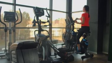 Spor salonunda spor ayakkabılarıyla bisiklet süren genç aktif bir kadın. Hava bisikletinde kadın eğitimi.