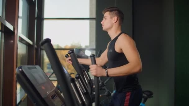 Achteraanzicht van een man in de cardio van de fitnesstreinen op een crosstrainer — Stockvideo