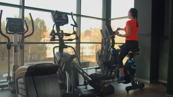 Jeune femme active faisant tourner un vélo pneumatique en salle de gym avec des entraîneurs. Entraînement féminin sur vélo pneumatique . — Video