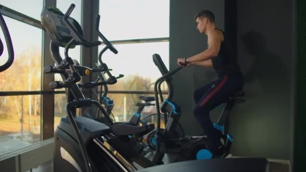 Ajustez les jeunes hommes utilisant le vélo pneumatique à la salle de gym. Athlète masculin fort faisant de l'entraînement cardio sur le cycle au club de santé . — Video