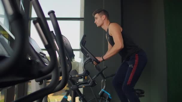 Krásný fit sportovní pozitivní mladý muž v tělocvičně dělá cvičení na eliptické trenér cvičení ven. Hard — Stock video