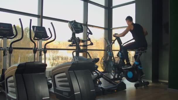 Joven hombre activo girando una bicicleta de aire en el gimnasio con entrenadores. entrenamiento masculino en bicicleta neumática — Vídeos de Stock