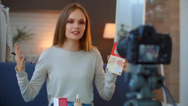 Ένα όμορφο νεαρό κορίτσι makeup blogger μιλά για την τεχνική της χρήσης πινέλα highlighter και σκιές για να δημιουργήσετε μακιγιάζ. κάμερα σε τρίποδο καταγράφει τη συνέντευξη. — Αρχείο Βίντεο