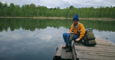 Güzel bayan gezgin ya da sırt çantalı gezgin muhteşem doğa manzarasında dinleniyor. Tatillerde eşsiz yeşil dağ gölünden gelen çay ve içeceğin tadını çıkarıyor.