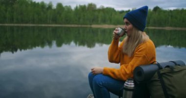 Güzel bayan gezgin ya da sırt çantalı gezgin muhteşem doğa manzarasında dinleniyor. Tatillerde eşsiz yeşil dağ gölünden gelen çay ve içeceğin tadını çıkarıyor.