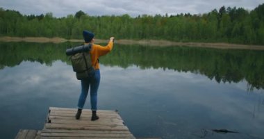 Yürüyüşçü kadın göl manzaralı akıllı telefonla fotoğraf çekiyor. Turist fotoğraf uygulaması kullanıyor, ekrana dokunuyor. Slow Motion 120 fps dengelendi. Destansı Steadicam çekimi.