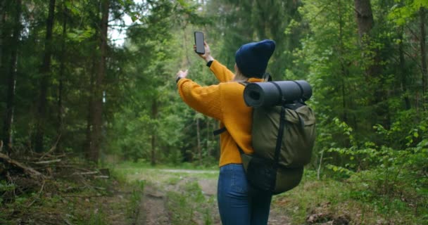 Slow motion: Jonge vrouw wandelaar met behulp van haar smartphone, terwijl ze geniet van haar weekend in het bos. Reizende vrouw met rugzak wandelend op pad door het bos kijkend naar de telefoon en kaart in groen hout — Stockvideo
