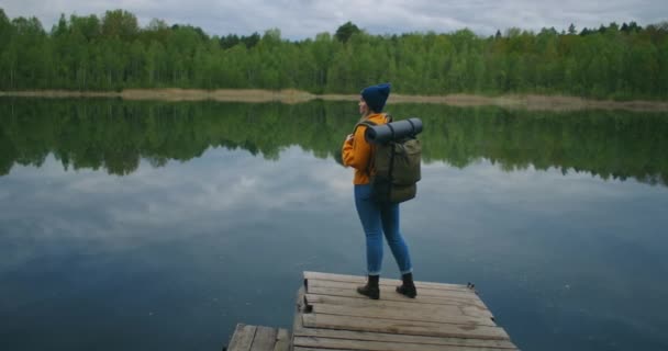 白人妇女在森林中著名的湖边游览。秋天和夏天在森林里旅行和探险的概念。女人看着森林湖中的十字架 — 图库视频影像
