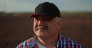 Ağır çekimde beyzbol şapkalı bir erkek çiftçi iş gününden sonra gün batımını seyrediyor..