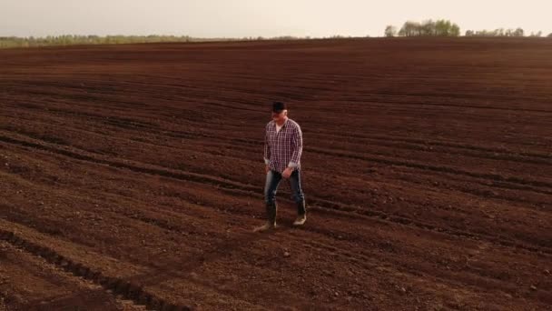 Filmagem aérea um fazendeiro idoso caminha através de um campo com terra arada em suas botas em câmera lenta — Vídeo de Stock