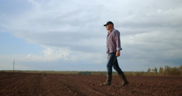 Pomalý pohyb: starší samec, řidič traktoru, projde po práci zoraným polem — Stock video