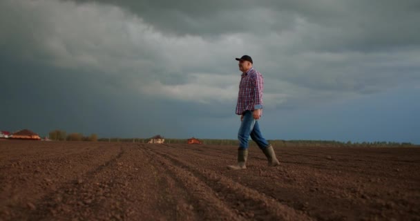 Movimento lento: macho sênior um motorista de trator caminha através de um campo arado ao pôr do sol após o trabalho — Vídeo de Stock