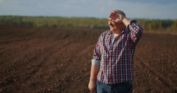 Um agricultor do sexo masculino tira o boné de basebol e olha para o pôr do sol depois de um dia de trabalho . — Vídeo de Stock