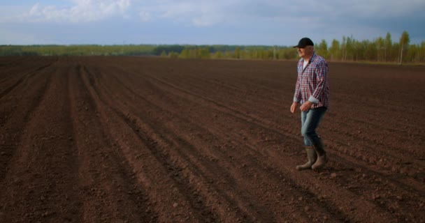 Чоловік фермер ходить полем з оранкою землі в чоботях у повільному русі — стокове відео