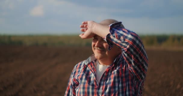 Agricultor sênior em um campo olhando para a distância. Agricultor sênior em pé no campo de soja examinando a cultura ao pôr do sol — Vídeo de Stock