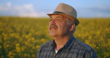 Son sınıf Kafkasyalı kameraya bakıyor şapkalı akıllı bir çiftçi yan tarafa bakıyor, yüzünü kameraya çeviriyor ve buğday tarlasında gülümsüyor. Portre