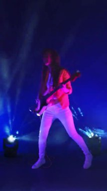 Neon ışıklı bir stüdyoda gitarlı komik bir kadının dikey videosu.