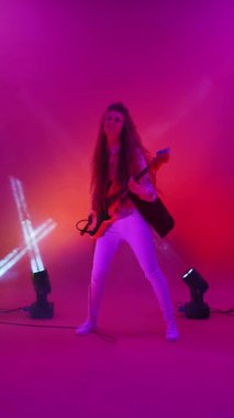 Dans eden neşeli bir kadının arka plandaki ışıkta gitar çalmasının dikey videosu.