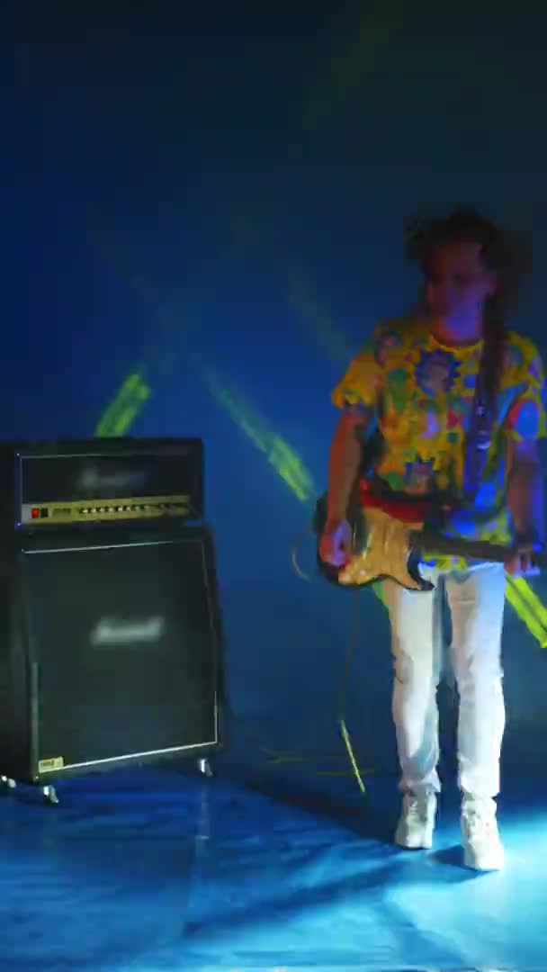 Video vertikal dari gitaris rock lompat gila dengan gitar di tangannya pada warna neon latar belakang menari dan bermain gitar. Cahaya konser — Stok Video