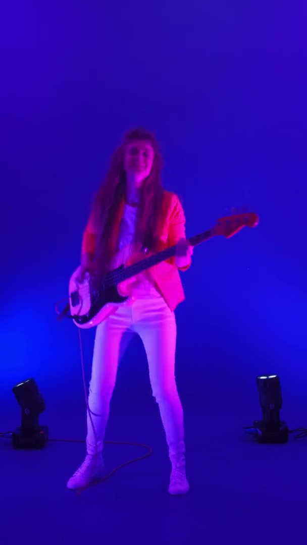 Vertical video of a woman playing bass guitar in a Studio dancing and looking at the camera — Stock Video