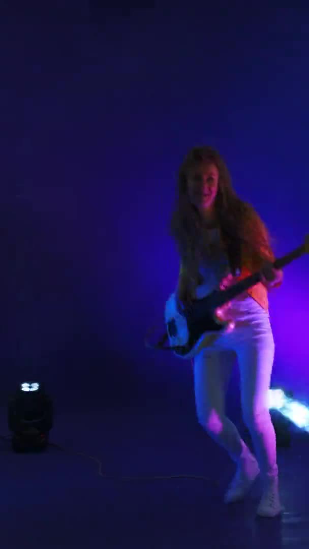 Vidéo verticale femmes folles musicienne rock jouant de la guitare en studio à la lumière des projecteurs et de la fumée dansant et sautant en studio — Video