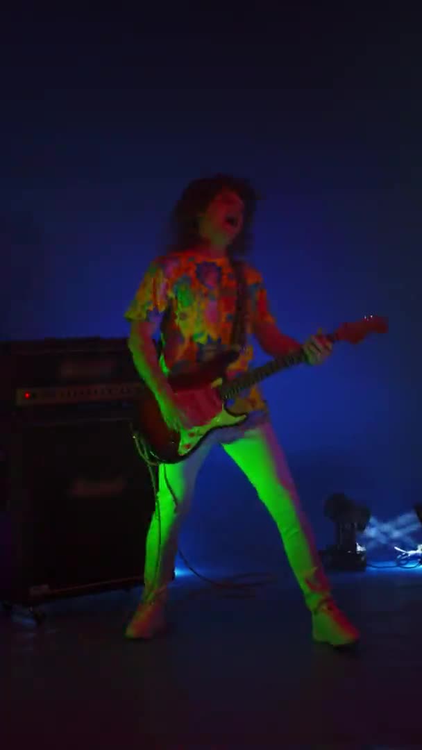 Vertical video of a dancing gay man playing guitar on a changing background light and strobe lights of a concert light. Bright neon lights — Stock Video