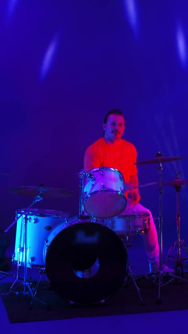 冷冰冰的摇滚音乐人在舞台上打鼓，在俱乐部霓虹灯和蓝灯的照耀下，表演了一个令人惊奇的金属独奏. — 图库视频影像