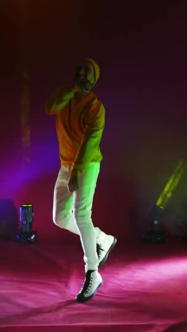 Vidéo verticale. Un chanteur en costume jaune danse et chante avec un microphone en couleur néon. Saute et bouge vigoureusement. — Video