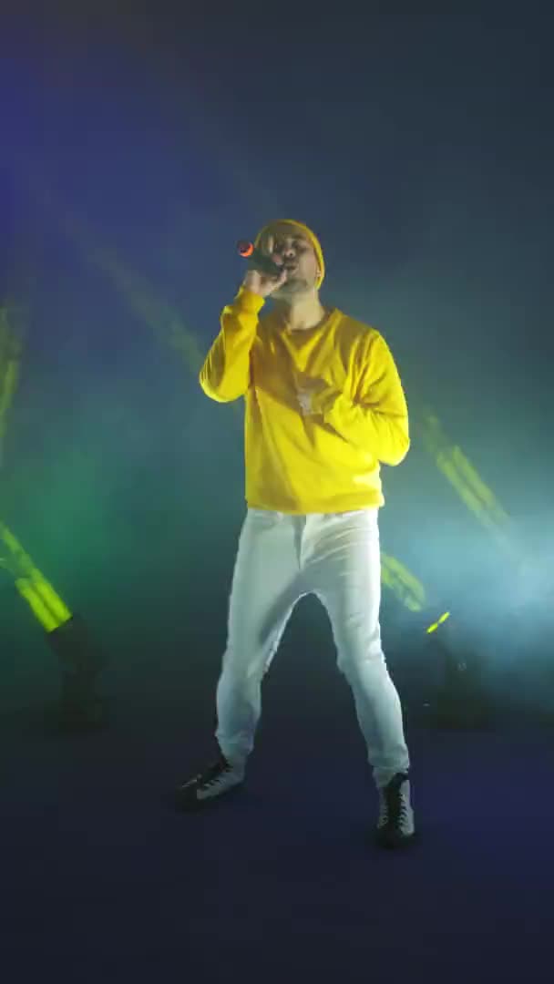 Video verticale. Un cantante in tuta gialla balla e canta con un microfono di colore neon. Salta e muoviti vigorosamente . — Video Stock
