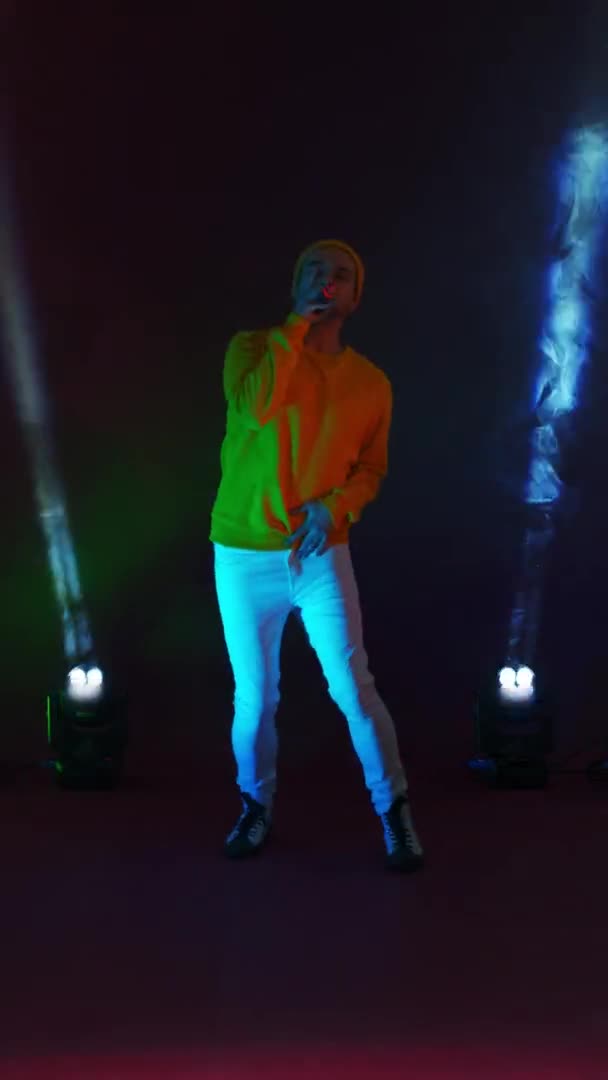 Vertical video. Incendiary funny Singer in yellow clothes dancing and singing with a microphone in neon color. Jump and move vigorously. Hip-hop and pop artist — Stock Video