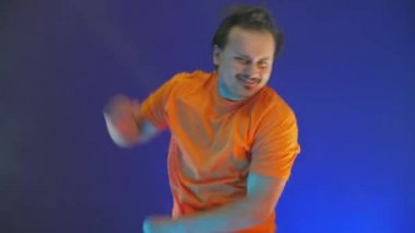 Aktif atlayan adam kameraya bakıyor. Çılgın adam dansın neon ışığında dans ediyor. Renkli mavi arka plandaki komik adam..