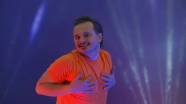 Aktif atlayan adam kameraya bakıyor. Çılgın adam dansın neon ışığında dans ediyor. Renkli mavi arka plandaki komik adam..