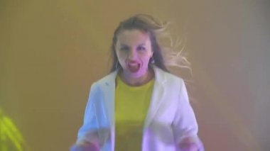 Enerjik, pozitif bir kadın stüdyoda sarı bir arka planda neşeyle dans ediyor ve kameraya bakarken çığlık atıyor. Başarı ve neşe. Mutluluk kavramı.