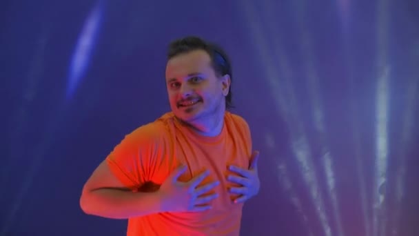 Un uomo che salta guardando la telecamera. Pazzo che balla nella luce al neon del ridicolo ballo. Uomo divertente su uno sfondo blu colorato . — Video Stock