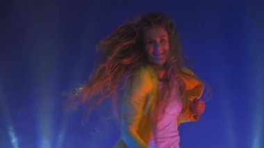 Sarı ceketli komik bir kadın neon ışıkta atlar ve dans eder.