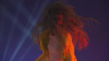 Uzun saçlı, eğlenceli, gülümseyen, stüdyoda mavi arka planda dans eden tuhaf bir kadın. Müzik, dans konsepti