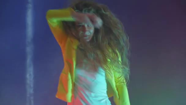 A funny woman in a yellow jacket jumps and dances energetically in the neon light and smoke — Stock Video