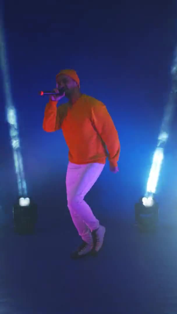 Vertical video. A man in a yellow jacket dancing on a blue background. Singer in the Studio in neon light dancing and singing — Stock Video