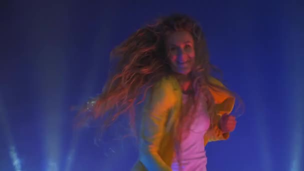 黄色のジャケットの面白い女性がジャンプし、ネオンの光と煙の中で精力的に踊ります — ストック動画