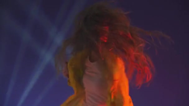 Femme insolite drôle aux cheveux longs s'amusant, souriant, dansant en studio sur fond bleu. Musique, concept de danse