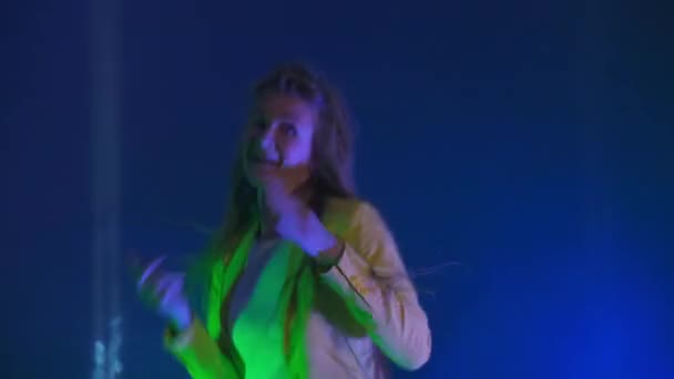 A mulher dança alegremente e olha para a câmera à luz de luzes estroboscópicas e holofotes. Cores de néon e garota louca dançando à música e cantando — Vídeo de Stock