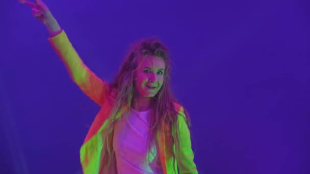 Žena vesele tančí a dívá se do kamery ve světle záblesků a reflektorů. Neonové barvy a bláznivá dívka tančí na hudbu a zpěv — Stock video