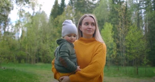 Una giovane madre cammina insieme nel parco con un bambino che la tiene tra le braccia. Abbraccia tuo figlio e cammina insieme nel bosco . — Video Stock