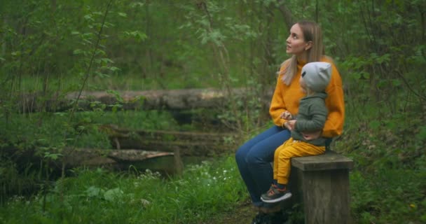 Une mère et son jeune fils sont assis sur un banc dans le parc et parlent. La mère explique au petit garçon répondant à des questions curieuses. — Video