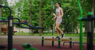 Parktaki genç bir kadın yaz aylarında spor kıyafetleriyle bankta yürüyüş egzersizleri yapıyor..