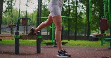 Genç ve güzel bir kadın yaz aylarında parkta bir bankta egzersiz yapıyor. Yazın parkta sağlıklı bir yaşam tarzı ve spor eğitimi..
