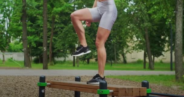 Mladá žena v parku provádí cvičení chůze na lavičce ve sportovním oblečení v létě. — Stock video