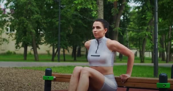 Een vrouwelijke atleet oefent in slow motion omgekeerde oefeningen uit op een bank in een park. Mooie vrouw die sport in het park — Stockvideo