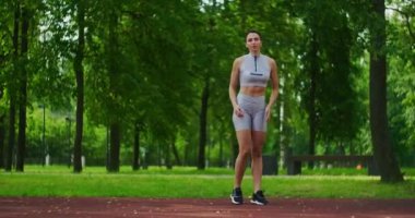 Kadın sporcu yan hamleler yapıyor bacaklarını çalıştırıyor ve yavaş çekimde parka atlıyor. Parkta spor yapan güzel bir kadın..