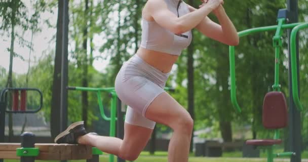 Лёгкая атлетика тренируется в парке на скамейке, выполняя выпады приседает на одну молодежь — стоковое видео